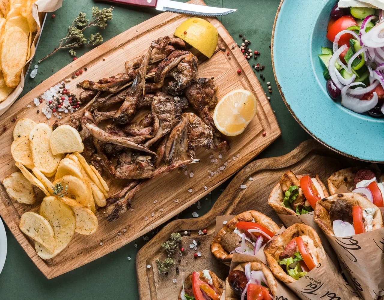Grilled lamb chops on a wooden board with lemon and crisps, a Greek salad, and wrapped pitas at Tsi Tsi in Glyfada